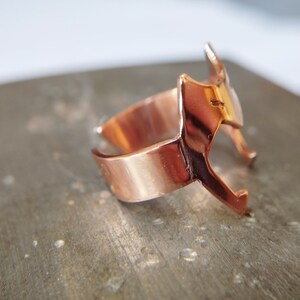 Peut inclure: Une bague en cuivre avec un design g&eacute;om&eacute;trique. La bague est ouverte d'un c&ocirc;t&eacute; et a une finition lisse et polie.