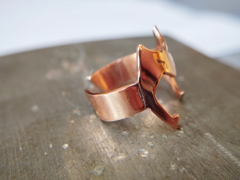 Peut inclure: Une bague en cuivre avec un design g&eacute;om&eacute;trique. La bague est ouverte d'un c&ocirc;t&eacute; et a une finition lisse et polie.