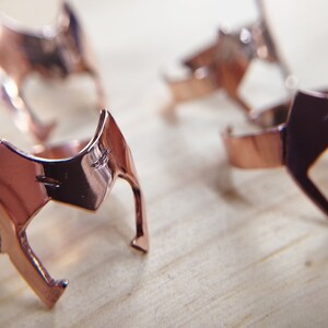 Peut inclure: Quatre bagues en or rose avec un design g&eacute;om&eacute;trique. Les bagues sont empil&eacute;es sur une surface en bois.