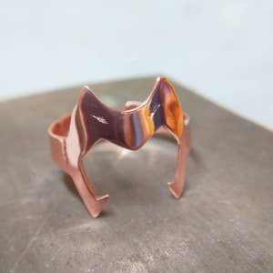 Peut inclure: Une bague en cuivre avec un motif de t&ecirc;te de renard stylis&eacute;. La bague est polie et a un &eacute;clat m&eacute;tallique chaud.