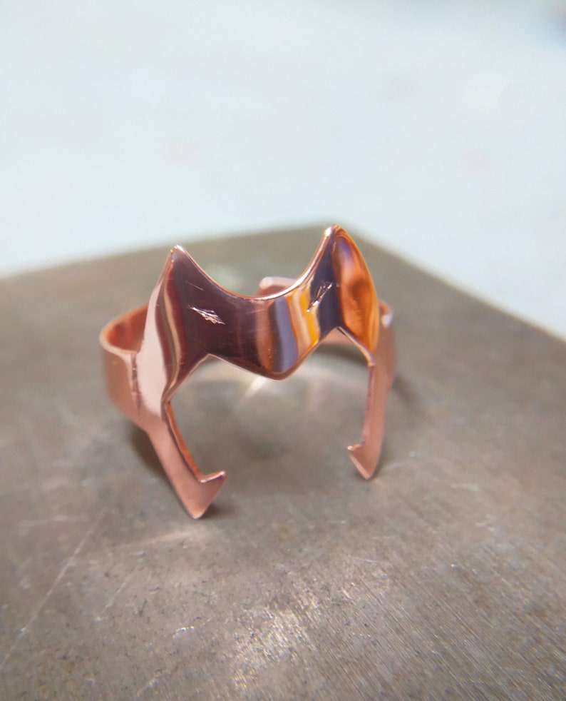 Peut inclure: Une bague en cuivre avec un motif de t&ecirc;te de renard stylis&eacute;. La bague est polie et a un &eacute;clat m&eacute;tallique chaud.