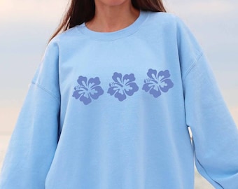 May include: A light blue sweatshirt with three purple hibiscus flowers printed on the front.