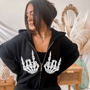 May include: Black hooded sweatshirt with a white skeleton hand graphic. The hands are making a rock and roll hand gesture.