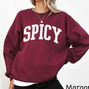 May include: A maroon sweatshirt with the word "SPICY" printed in white on the front.