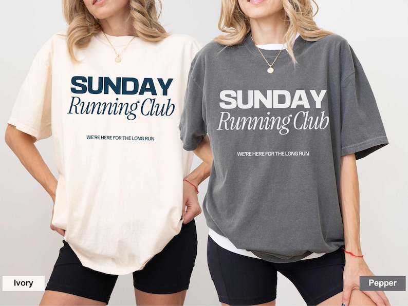 Puede incluir: Dos camisetas con el texto "SUNDAY Running Club" en diferentes colores. La camiseta de la izquierda es de color marfil con texto azul marino. La camiseta de la derecha es gris con texto blanco. Ambas camisetas tienen el texto "WE'RE HERE FOR THE LONG RUN" debajo del texto principal.