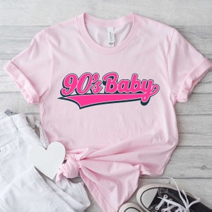 May include: Pink t-shirt with a pink and black graphic that says "90's Baby" in a retro baseball font.