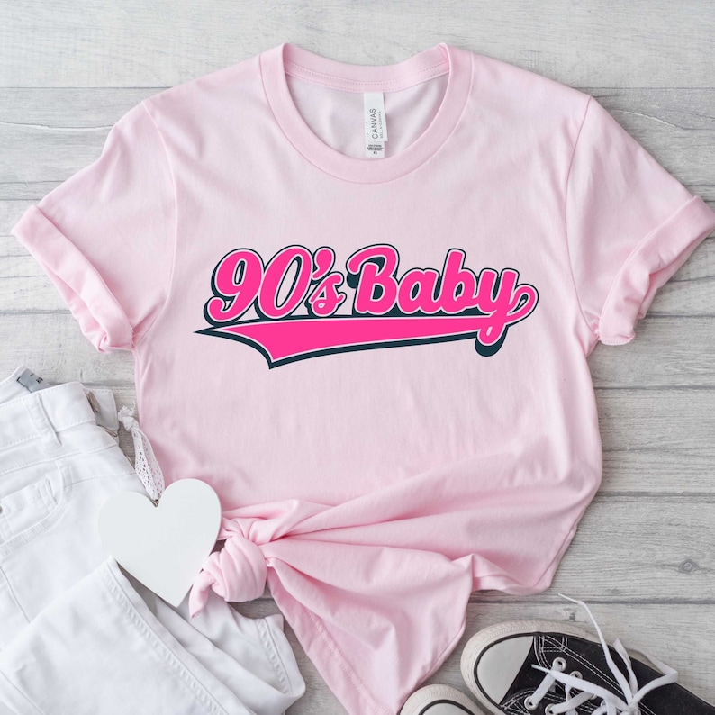 May include: Pink t-shirt with a pink and black graphic that says "90's Baby" in a retro baseball font.