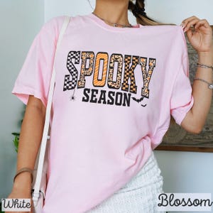 Może przedstawiać: Jasnor&oacute;żowa koszulka z napisem "SPOOKY SEASON" w czarno-pomarańczowo-białym wzorze. Słowo "SPOOKY" ma wz&oacute;r w kratkę i lamparci. Pająk i nietoperze są r&oacute;wnież zawarte w projekcie.