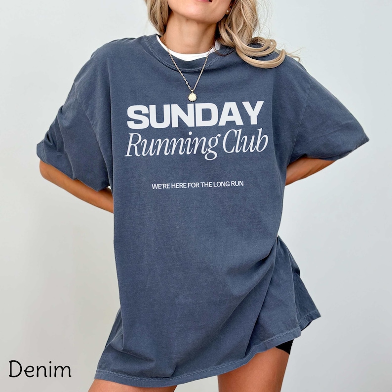 Puede incluir: Una camiseta de gran tama&ntilde;o de color azul oscuro con el texto "SUNDAY Running Club" y las palabras "WE'RE HERE FOR THE LONG RUN" en blanco. La camiseta est&aacute; hecha de un material suave y c&oacute;modo.