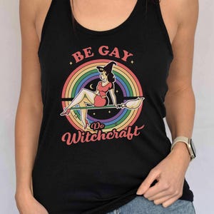 May include: Black tank top with a rainbow and a witch on a broomstick. The text on the shirt says "Be Gay Do Witchcraft".