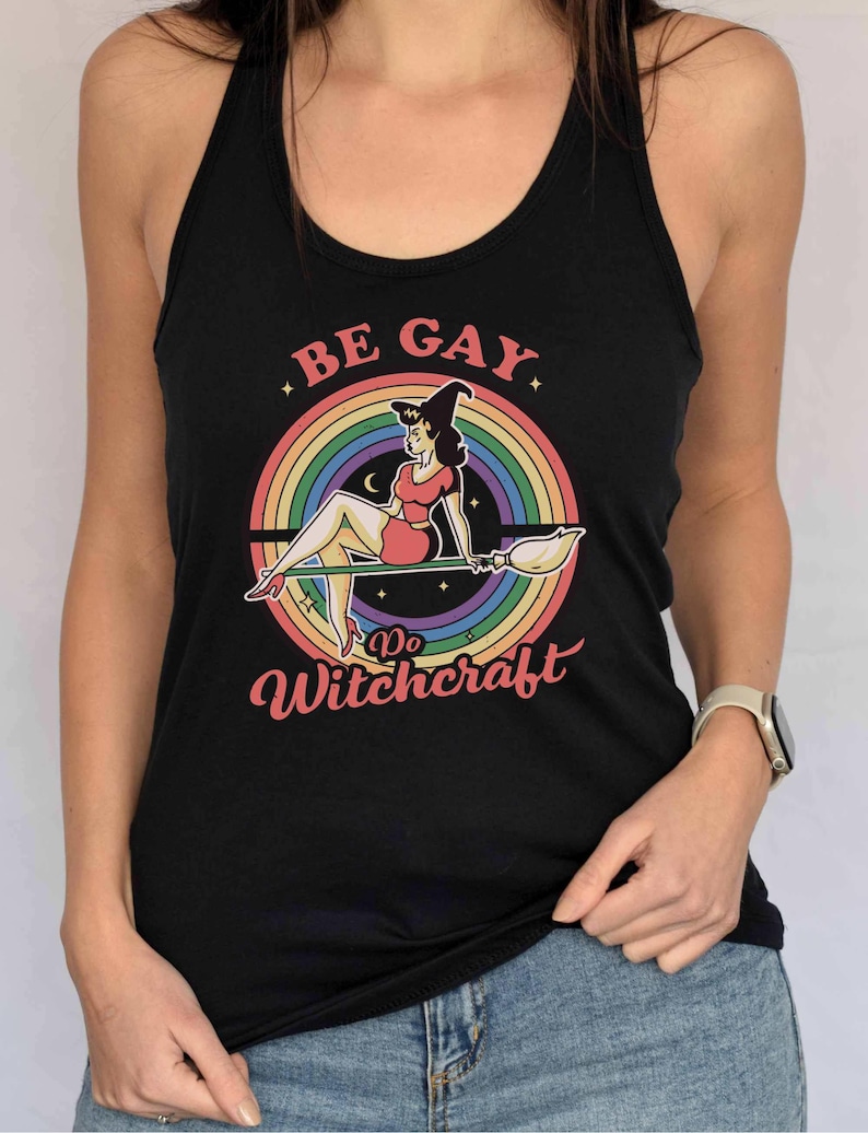 May include: Black tank top with a rainbow and a witch on a broomstick. The text on the shirt says "Be Gay Do Witchcraft".