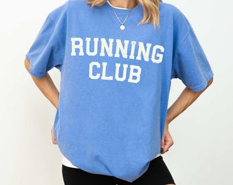 May include: A blue oversized t-shirt with the text "RUNNING CLUB" printed in white. The shirt is made of a soft, comfortable material and has a relaxed fit.