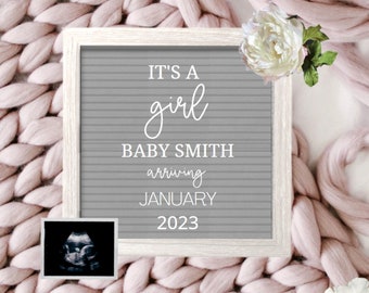 Może przedstawiać: Szara tablica z białymi literami, na której napisano "To dziewczynka, Baby Smith przybywa w styczniu 2023". Tablica jest otoczona różowym dzianym kocem i białymi kwiatami.