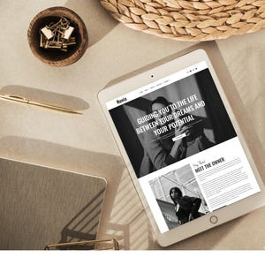 May include: A tablet displaying a website with the text "Guiding you to the life between your dreams and your potential." A gold pen, a small wooden bowl with gold paper clips, and a notebook are also on the beige surface.