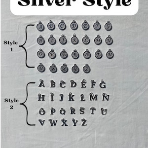 Pu&ograve; includere: Ciondoli Silver Style che mostrano l'alfabeto in due stili. I ciondoli in stile 1 sono circolari con una lettera al centro. I ciondoli in stile 2 sono lettere a blocchi. L'immagine contiene il testo "Silver Style".