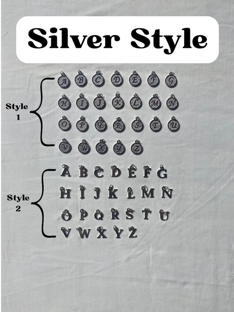 Pu&ograve; includere: Ciondoli Silver Style che mostrano l'alfabeto in due stili. I ciondoli in stile 1 sono circolari con una lettera al centro. I ciondoli in stile 2 sono lettere a blocchi. L'immagine contiene il testo "Silver Style".