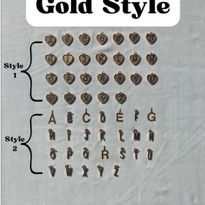 Pu&ograve; includere: Ciondoli color oro in due stili. Lo stile 1 presenta ciondoli a forma di cuore con le lettere A-Z. Lo stile 2 include singole lettere d'oro A-Z. Il testo "Gold Style" &egrave; in alto.