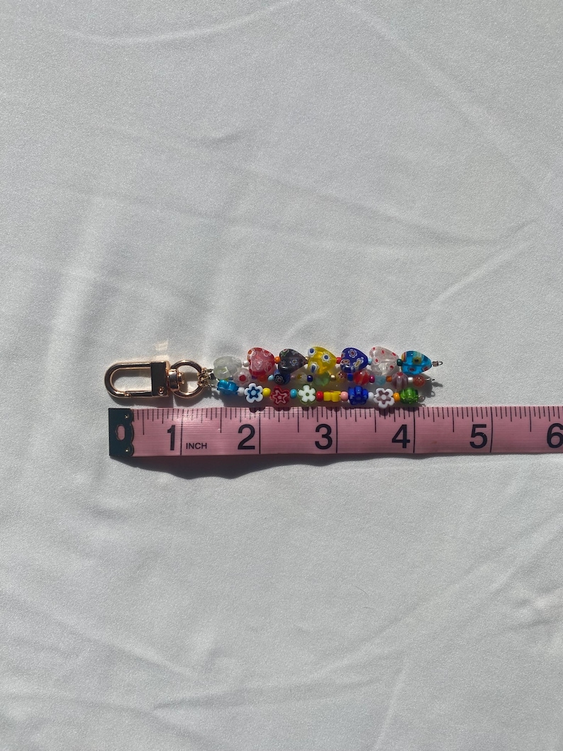 Pu&ograve; includere: Un portachiavi di perline con chiusura color oro. Il portachiavi &egrave; decorato con perline colorate, tra cui perline a forma di cuore e di fiore. Il portachiavi misura circa 10 cm di lunghezza.