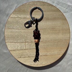 May include: A black and brown beaded keychain with a silver key ring. The keychain is hanging from a wooden surface.