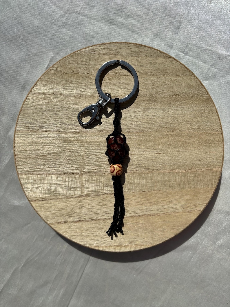 May include: A black and brown beaded keychain with a silver key ring. The keychain is hanging from a wooden surface.