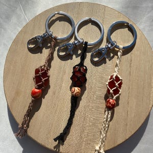 May include: Three keychains with red and brown stone beads, each with a different colored macrame cord: brown, black, and cream.