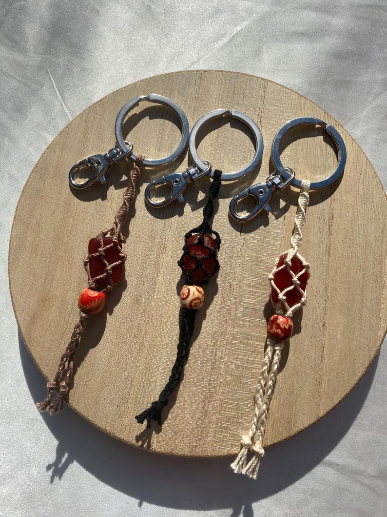 May include: Three keychains with red and brown stone beads, each with a different colored macrame cord: brown, black, and cream.