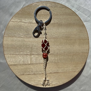 May include: A red and white macrame keychain with a red gemstone bead and a silver key ring.
