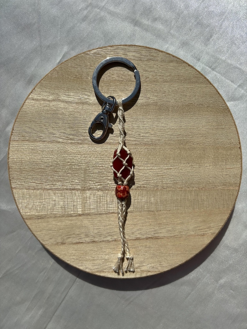 May include: A red and white macrame keychain with a red gemstone bead and a silver key ring.