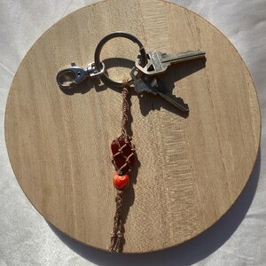 May include: A brown and red beaded keychain with a red stone charm and a silver key ring with three keys attached.