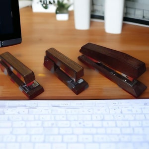 May include: Three wooden staplers in different sizes, with red and brown accents. The staplers are on a wooden surface with a white keyboard in the foreground.
