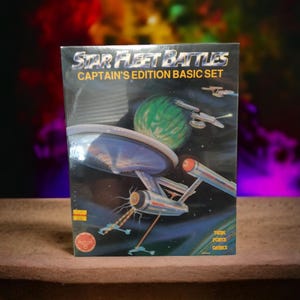 Puede incluir: Una caja para el juego de mesa Star Fleet Battles Captain's Edition Basic Set. La caja presenta una nave espacial en el espacio con un planeta verde en el fondo. La caja es de la empresa Trek Force Games.