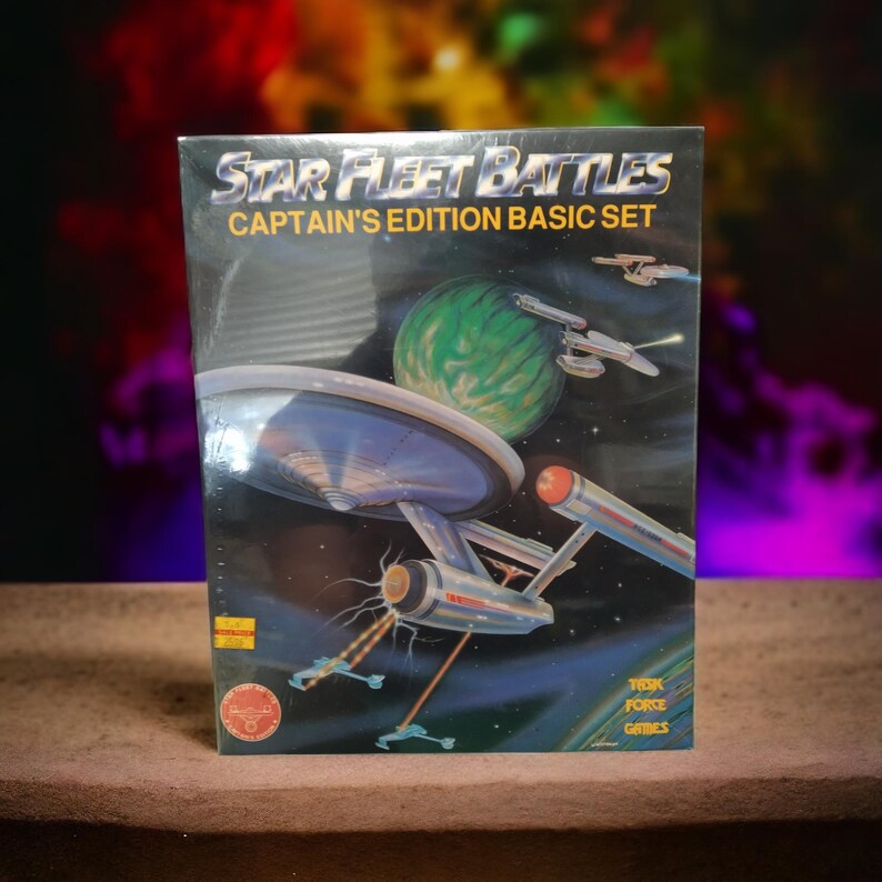 Puede incluir: Una caja para el juego de mesa Star Fleet Battles Captain's Edition Basic Set. La caja presenta una nave espacial en el espacio con un planeta verde en el fondo. La caja es de la empresa Trek Force Games.