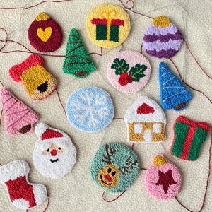 Op de afbeelding: Een verzameling van 14 handgemaakte kerstversieringen van vilt, waaronder een sneeuwpop, een rendier, een huis, een kerstboom, een sok, een cadeau en een sneeuwvlok. De versieringen zijn allemaal in verschillende kleuren en hebben verschillende ontwerpen.