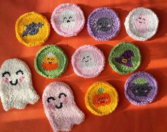 May include: A selection of handmade Halloween-themed coasters and ghost-shaped decorations. The coasters feature embroidered designs of a bat, candy corn, a witch's hat, a pumpkin, and smiling ghosts. The color palette includes yellow, pink, green, purple, and white.