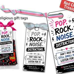 May include: Religious gift tags with the text "POP. ROCK. NOISE. DISTRACTIONS." and "DON'T MISS THE STILL SMALL VOICE. LISTEN FOR IT." One tag is attached to a bag of popping candy. The tags have pink, gray, and white ribbons.