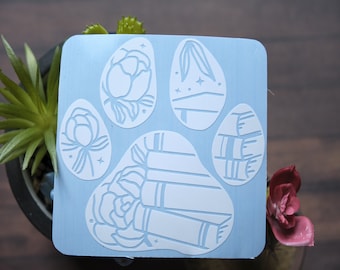 May include: A light blue paw print stencil with five sections. Each section features a white design of a flower, bamboo, or a stack of books.