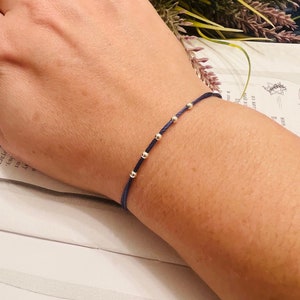 May include: A navy blue string bracelet with silver beads. The bracelet is on a person's wrist.
