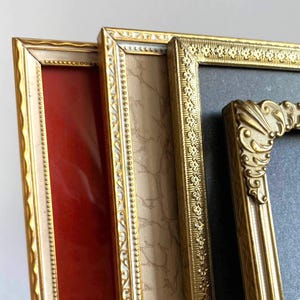 Può includere: Primo piano di tre cornici per foto vintage. Le cornici hanno bordi dorati ornati e interni di diversi colori, tra cui rosso, beige e nero. Le cornici sono disposte ad angolo, mostrando i loro dettagli decorativi.
