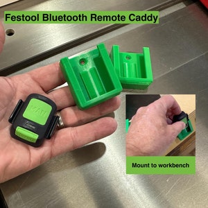 May include: Green plastic caddy for a Festool Bluetooth remote. The caddy is designed to mount to a workbench. The remote is black with green buttons and the text "MAN" on the front.