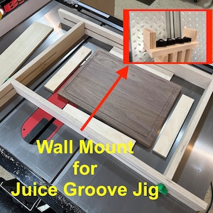 May include: A wall mount for a juice groove jig. The jig is made of wood and has a metal clamp. The jig is mounted on a table saw. The text "Wall Mount for Juice Groove Jig" is written on the table saw.