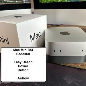 May include: A silver Mac Mini M4 computer with a white box that says "Mac mini" on it. The computer is on a pedestal that raises it up for easy access to the power button. The pedestal also helps with airflow.