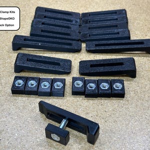 May include: A set of black CNC clamp kits with T-track option. The kit includes 12 clamps, 8 nuts, and 1 clamp with a screw. The text on the image reads "CNC Clamp Kits, Fits ShapeOKO, T-Track Option".