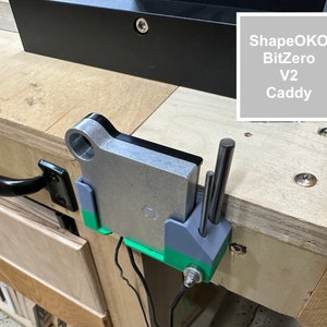 May include: A gray and green 3D printed bit holder with the text "ShapeOKO BitZero V2 Caddy" on a gray background.