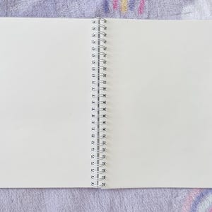 May include: A white spiral bound notebook with blank pages, open to a fresh page.