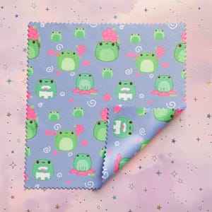 May include: A blue microfiber cleaning cloth with a repeating pattern of green frogs and pink flowers. The cloth is folded in half and has a scalloped edge.