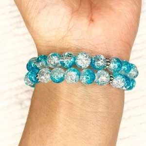 May include: A double-strand bracelet made of clear and blue glass beads with a speckled effect. The beads are round and have a silver-toned metal spacer between them.