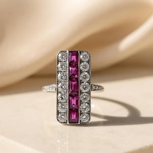Peut inclure: Une bague rectangulaire présentant une rangée verticale centrale de cinq rubis rose foncé taille baguette, flanquée de deux rangées verticales de cinq diamants ronds brillants transparents de chaque côté, sur une monture métallique polie.