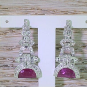 May include: A pair of dangle earrings with a pink gemstone and a silver setting. The earrings are decorated with small diamonds.