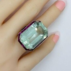 May include: A large, emerald-cut aquamarine ring set in a silver band with a pink ruby border.