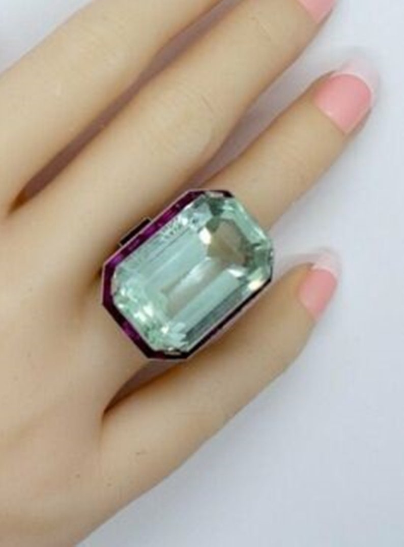 May include: A large, emerald-cut aquamarine ring set in a silver band with a pink ruby border.